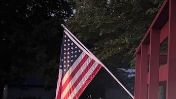 An American flag mounted on a flagpole in front of a red building.