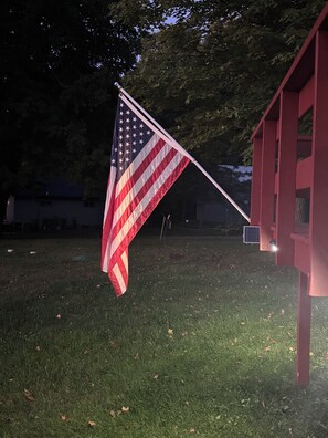 An American flag mounted on a flagpole in front of a red building. - The Lake Haus: Peaceful 2BR Waterfront Getaway on Elm Island Lake (Aitkin)