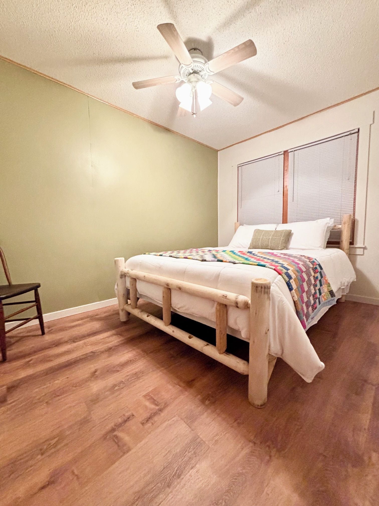 A bedroom with a wooden bed frame, a ceiling fan, a window with blinds, and a wooden floor.