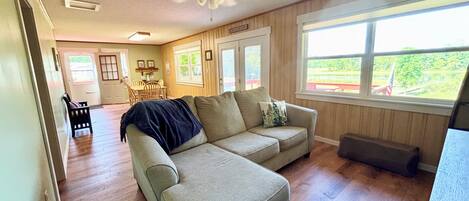 Ein Wohnzimmer mit einer Eckcouch, einem Deckenventilator, einem Essbereich mit Tisch und Stühlen und einem großen Fenster mit Aussicht.
