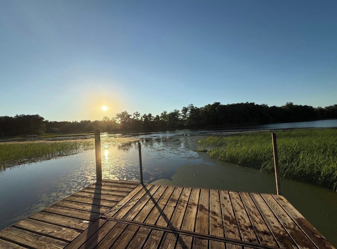 A wooden dock extending over a calm body of water with a sunrise in the background.
