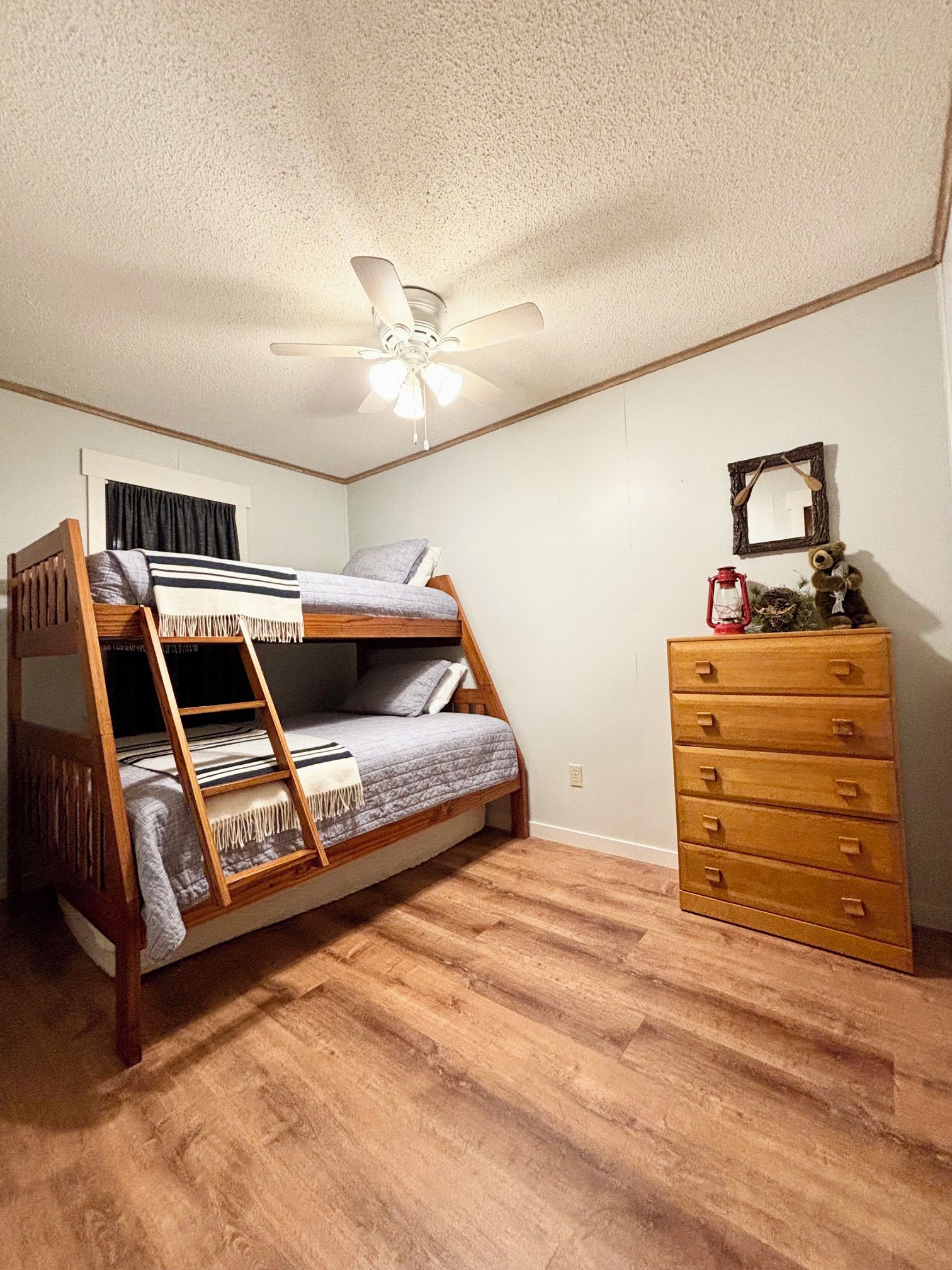 A room with a bunk bed, a wooden dresser, a ceiling fan, and a wall-mounted mirror.