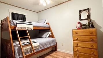 A room with a bunk bed, a wooden dresser, a ceiling fan, and a wall-mounted mirror.