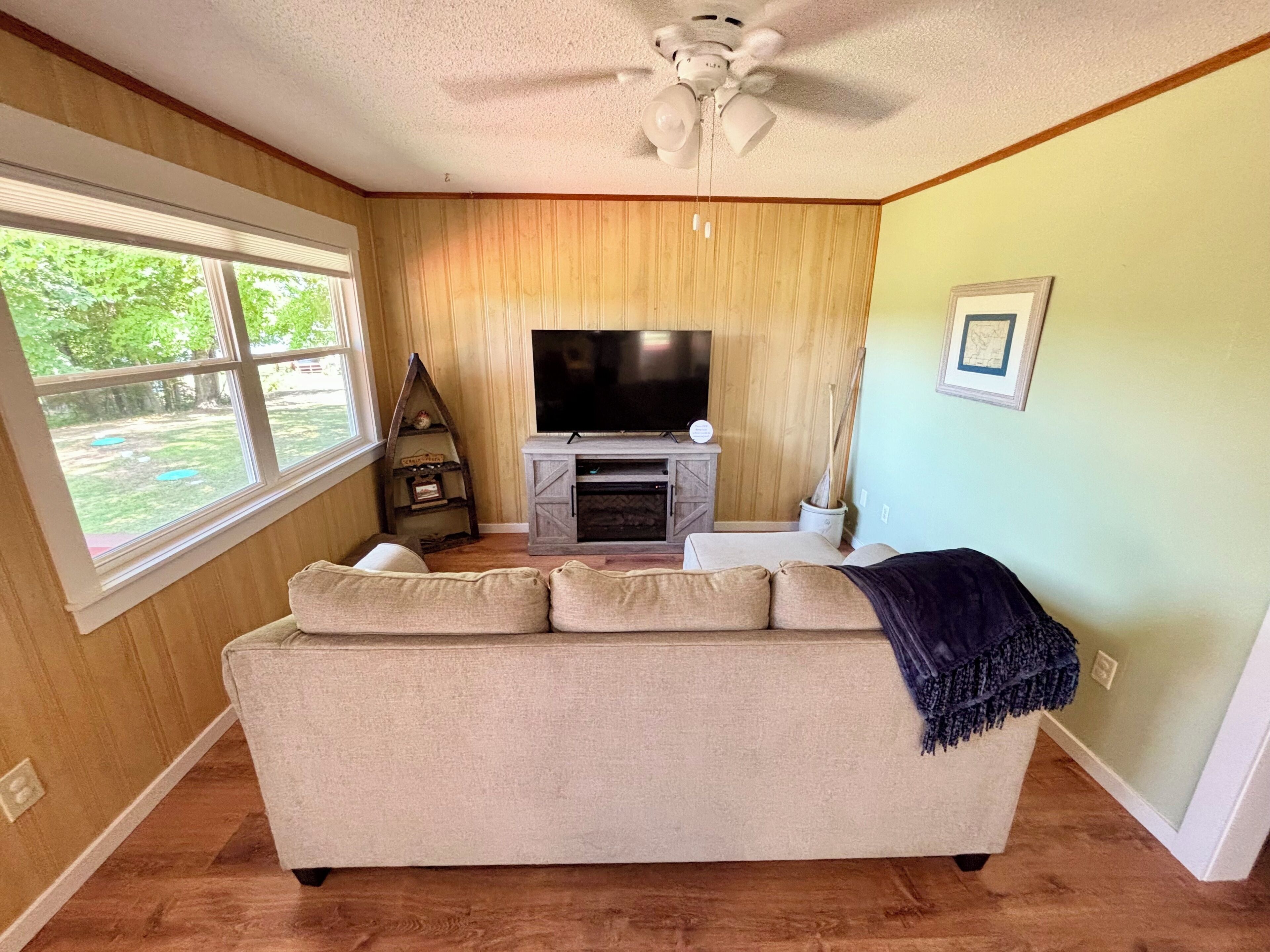 A living room with a beige sofa, a fireplace, a television, and a ceiling fan.