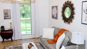 Ein Wohnzimmer mit grauem Sofa, weißen und orangefarbenen Kissen, einem runden Spiegel und einer Lampe.