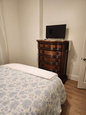 Een slaapkamer met een bed, een dressoir en een televisie bovenop het dressoir.