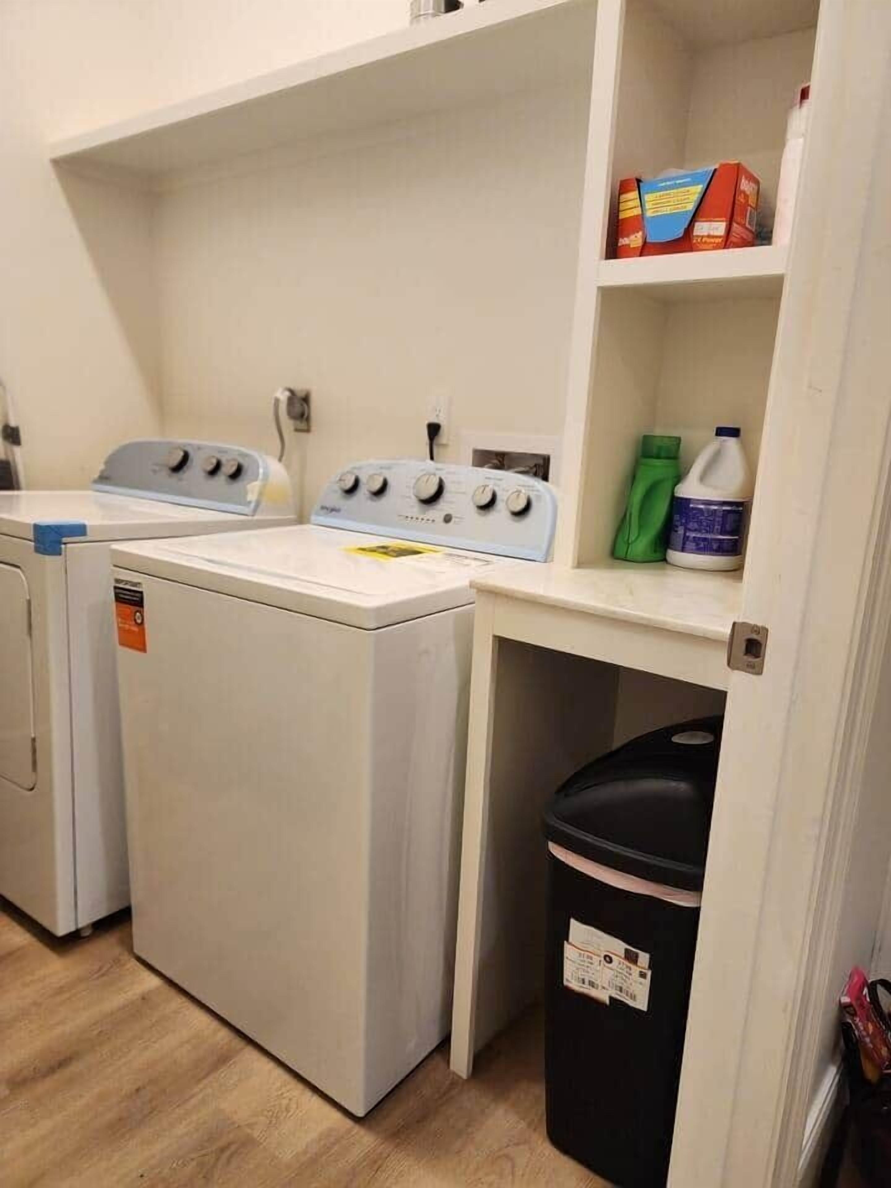 Een wasruimte met een wasmachine, droger en een plank met schoonmaakmiddelen.