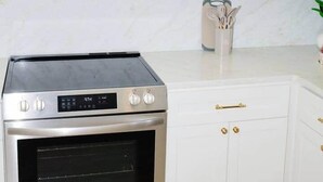 Eine Küche mit Edelstahlbackofen, weißen Schränken mit goldenen Griffen und einer Marmor-Spritzschutzwand.