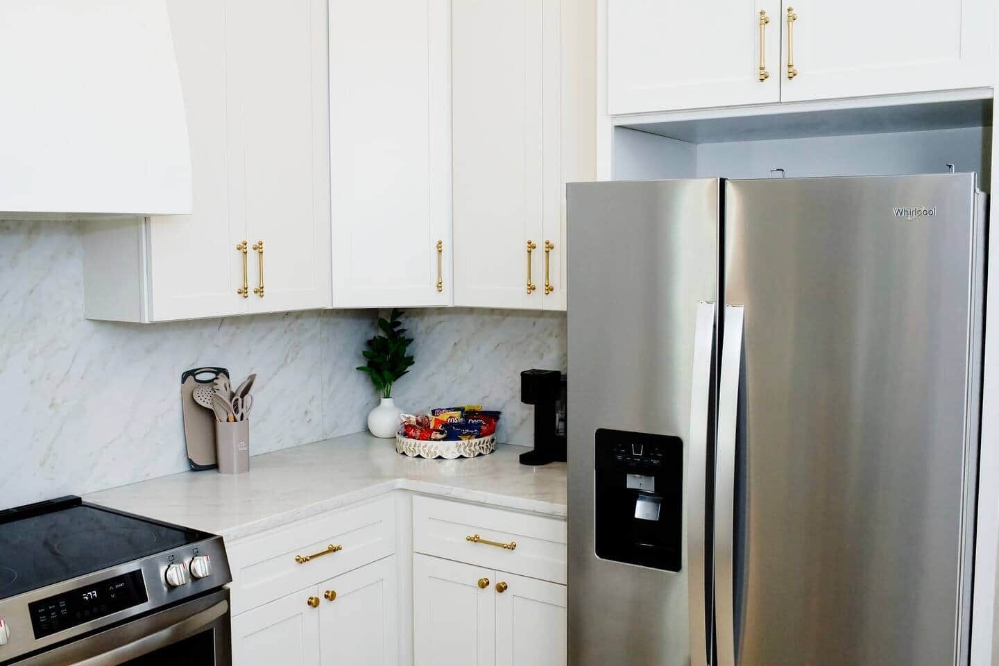 Une cuisine avec des meubles blancs, un réfrigérateur en acier inoxydable et une cuisinière à gaz.