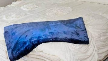 Een bed met een gestoffeerd hoofdbord, een witte spreideken en een blauw kussen.