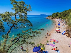 A beach with clear water, people sunbathing, and umbrellas. - für 2 Personen ca. 30 m² in Rijeka, Kvarner Bucht (Gespanschaft Primorje-G by Interhome (Rijeka)