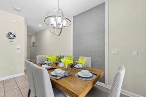 Un coin repas avec une table en bois dressée pour quatre personnes, entourée de chaises à revêtement blanc.