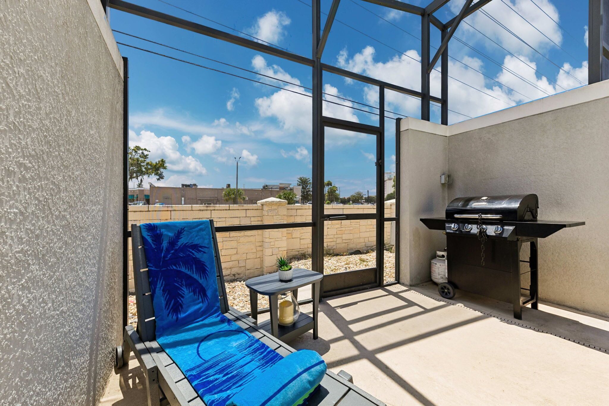 A covered outdoor area with a grill, a lounge chair, and a small table.