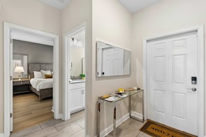 A hotel hallway with a bed, a mirror, a glass table with items, and a door with a keypad lock. - Brand New | 4Bd Private Pool, Resort Near Disney  4993 (Kissimmee)