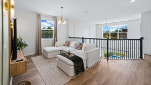 Uma sala de estar moderna com um sofá seccional, uma TV de tela plana e uma varanda com vista para a piscina.