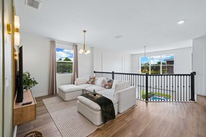 A modern living room with a sectional sofa, a flat-screen TV, and a balcony with a pool view. - Brand New 5BR 5BA Villa w Pool, Spa & Game Room 7800 (Kissimmee)
