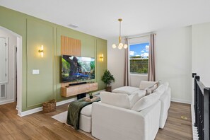 Una sala de estar moderna con un televisor de pantalla plana, un conjunto de sofás, un mueble de madera para entretenimiento y un amplio ventanal con cortinas.