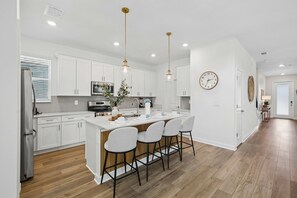 Una cocina moderna con armarios blancos, electrodomésticos de acero inoxidable y una isla central con taburetes de bar.