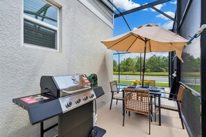 Eine Terrasss mit Grill, Esstisch, Stühlen und einem großen Sonnenschirm.