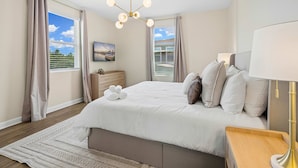 Quarto com cama, mesas de cabeceira, abajur, cortinas, televisão e vista para o exterior.