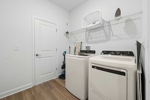 A laundry room with a door, two washing machines, a drying rack, and a vacuum cleaner. - Brand New 5BR 5BA Villa w Pool, Spa & Game Room 7800 (Kissimmee)