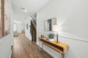 Un pasillo con piso de madera, una consola con lámpara, un espejo y una escalera.