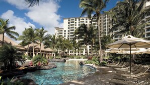 A resort pool area with lounge chairs and umbrellas, surrounded by palm trees and a large hotel building. - 2-bedroom Ocean View Sleeps 8 at Marriott's Ko Olina Beach Club (Kapolei)