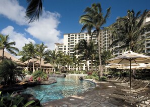 A resort pool area with lounge chairs and umbrellas, surrounded by palm trees and a large hotel building. - 2-bedroom Ocean View Sleeps 8 at Marriott's Ko Olina Beach Club (Kapolei)