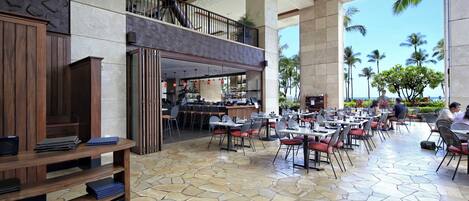 A spacious indoor area with a bar, seating, and a view of palm trees.