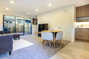 A modern living space with a dining area, a flat-screen TV, and a kitchen area with wooden cabinets.