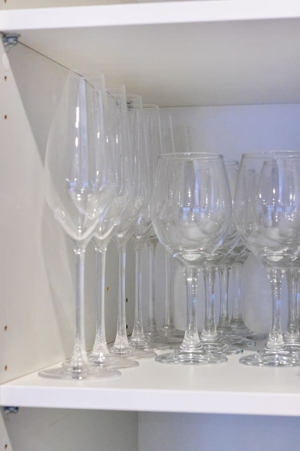 A shelf with multiple clear glass wine glasses.