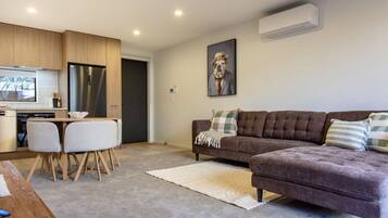 A modern living room with a sofa, a dining table, and a kitchen area with a refrigerator.