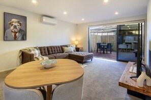 A modern living room with a sofa, a dining table, and a glass door leading to a patio.