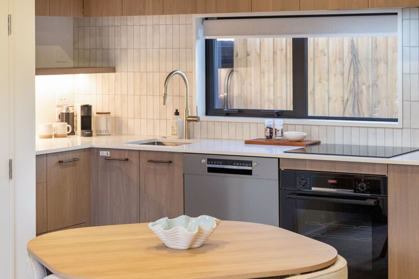 Ett modernt kök med diskmaskin, ugn och ett träbord med en skål.