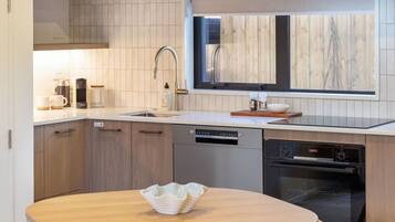 A modern kitchen with a dishwasher, oven, and a wooden table with a bowl.