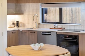 A modern kitchen with a dishwasher, oven, and a wooden table with a bowl.