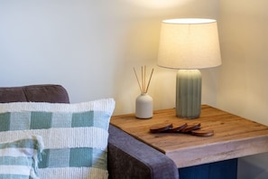 A neatly made bed with a striped pillow, a bedside table with a lamp, a vase, and a wooden tray.