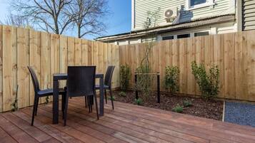 A wooden deck with a table and chairs, surrounded by a wooden fence and small plants.