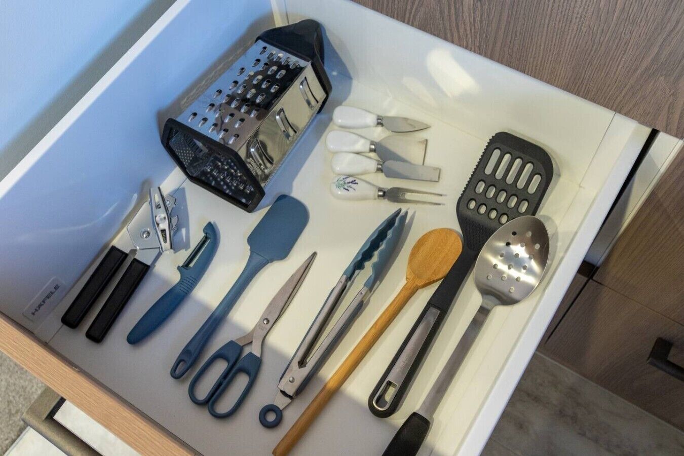 A drawer containing various kitchen utensils including scissors, a grater, and a spatula.