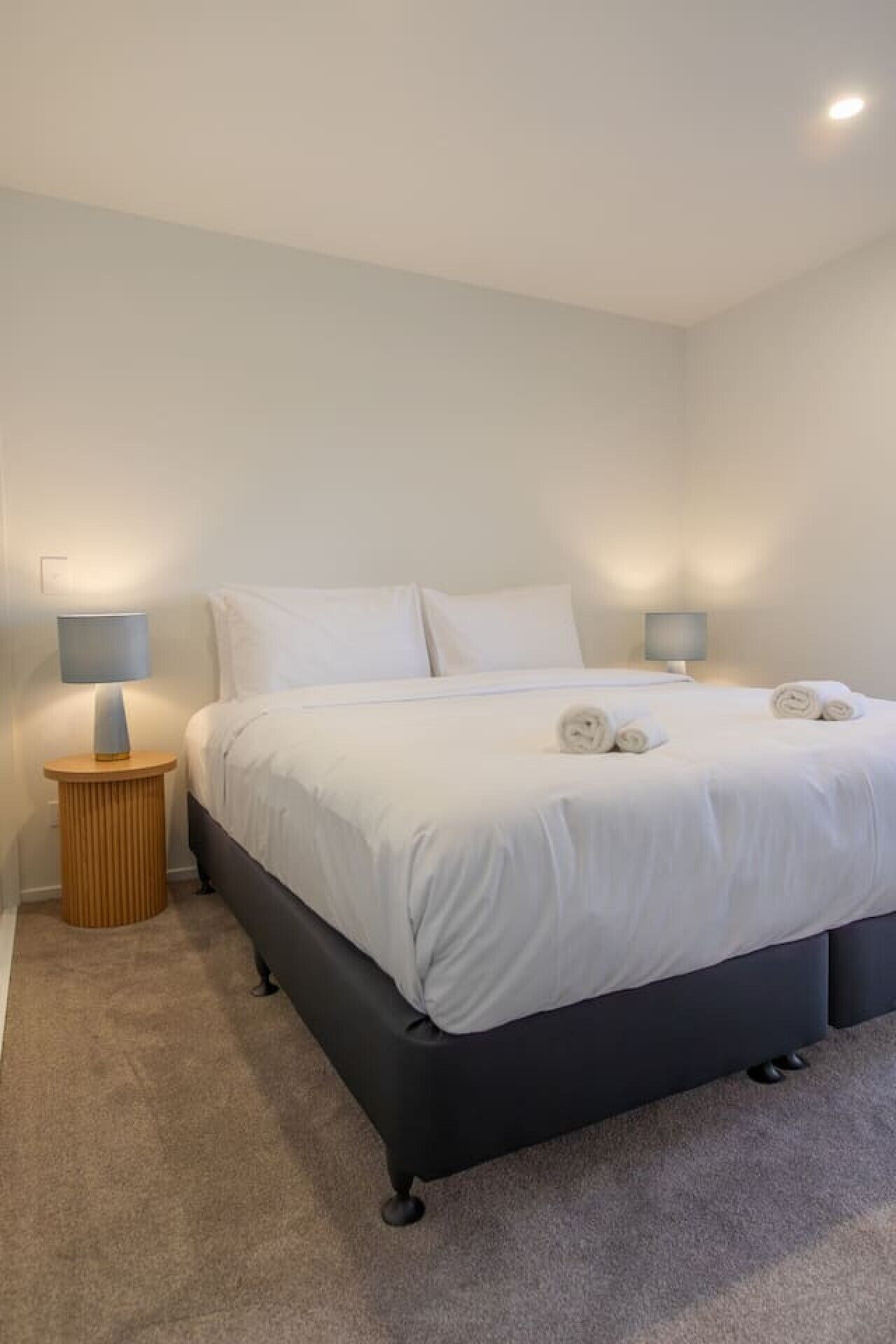 A modern bedroom with a bed, two bedside lamps, and a round wooden nightstand.