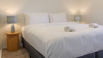 A modern bedroom with a bed, two bedside lamps, and a round wooden nightstand.