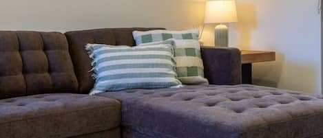 A living room with a brown sofa, striped pillows, a lamp, and a patterned rug.
