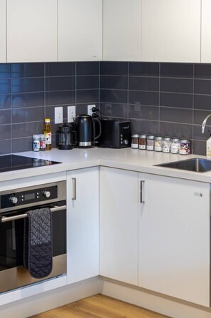 Une cuisine moderne équipée d’un four encastré, d’une machine à café et d’une bouilloire posées sur le plan de travail.