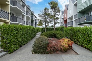 A residential building with multiple balconies, a central garden area with various shrubs, and a clear sky. - Ground Floor Apartment CBD - Pool, Gym + Parking (Christchurch)