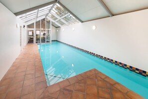 Une piscine intérieure avec un sol carrelé, un plafond en verre et une vue sur une autre pièce.