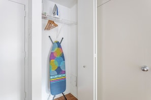 Ein Zimmer mit einer weißen Tür, einem an der Wand befestigten Bügelbrett mit farbigem Muster und einem Regal mit Bügeleisen und Holzaufhänger.