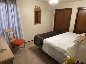 A bedroom with a bed, a chair, a desk, a lamp, and a window with curtains.