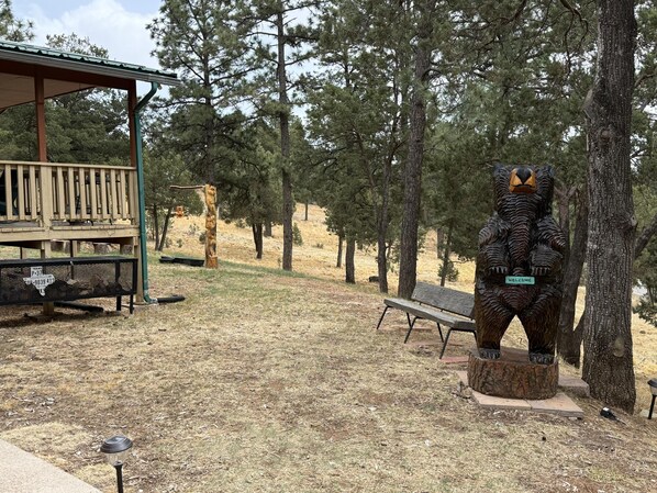 A wooden deck, a bench, and a bear statue in a park.