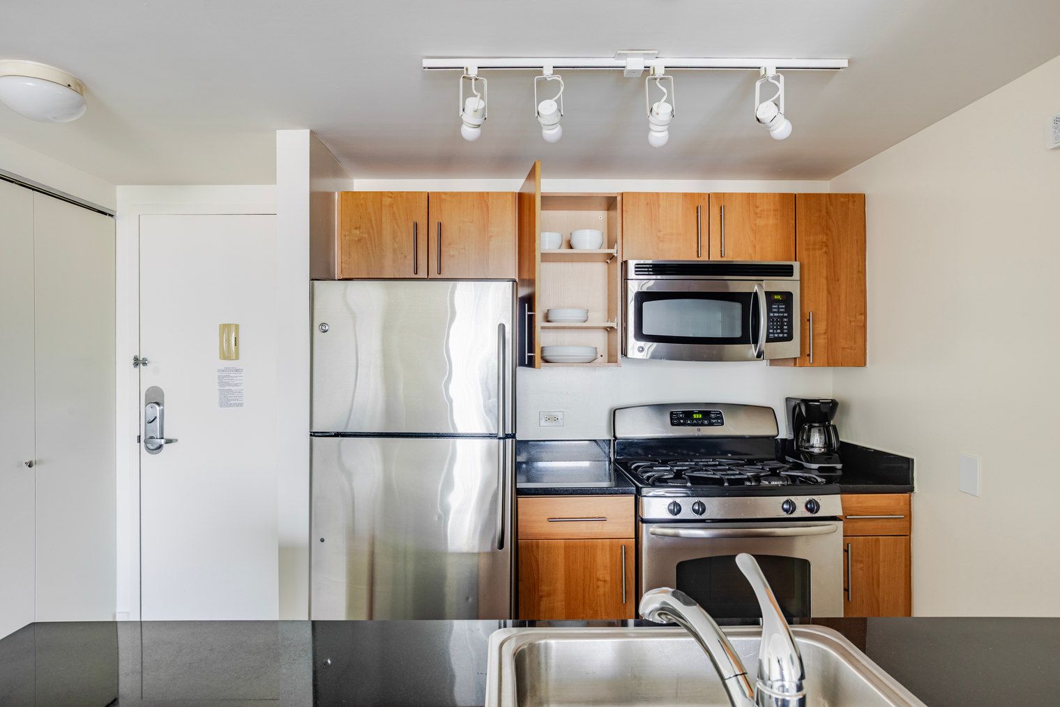A compact kitchen with stainless steel appliances, wooden cabinets, and a black countertop.