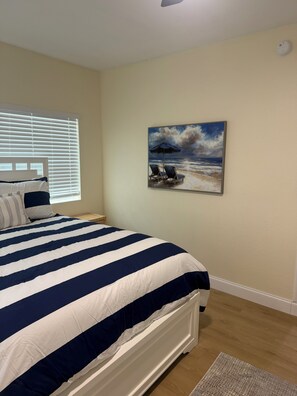 Een slaapkamer met een groot bed, een schilderij van een strand en een raam met zonwering.